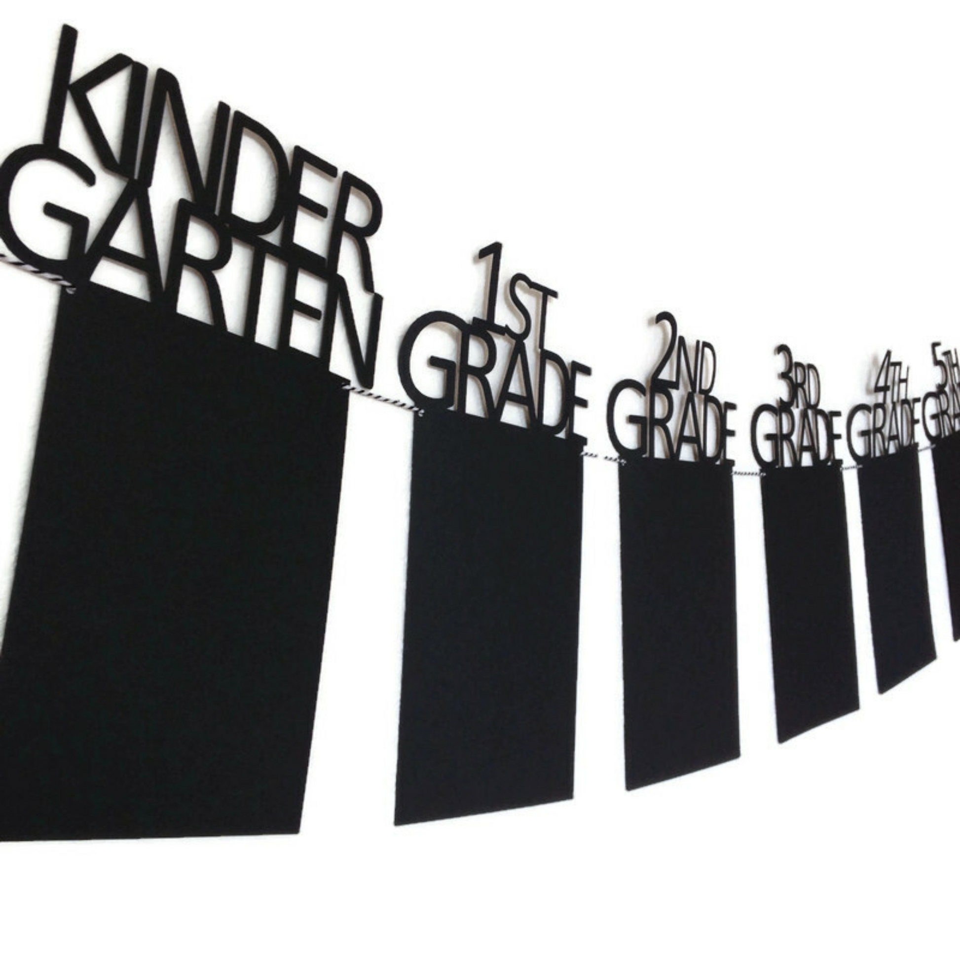 Black graduation banner with grades featuring kindergarten, first grade, and beyond. Strung on black and white twine and hanging on a white wall.