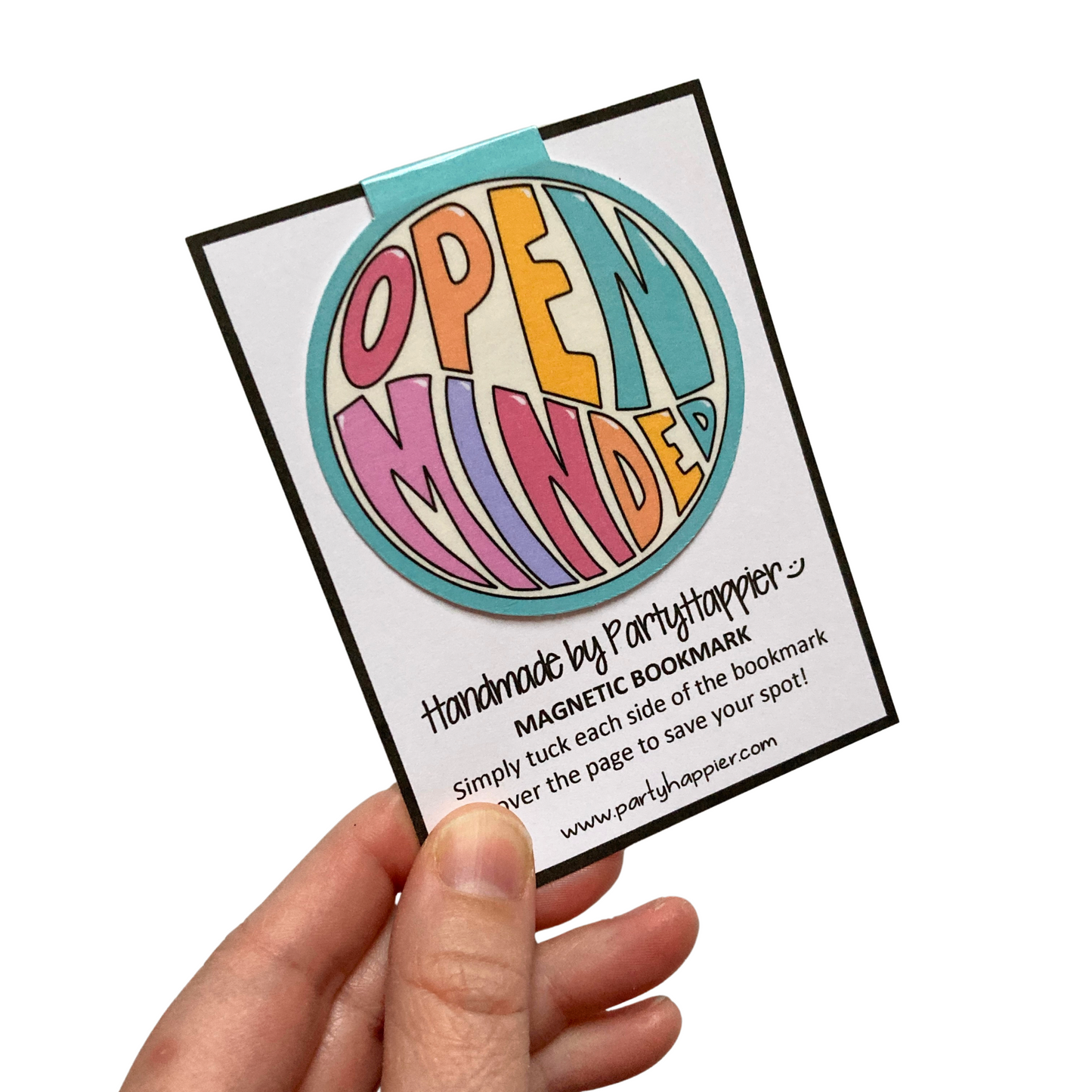 Hand holding round magnetic bookmark that is clipped onto packaging card. Bookmark features teal background and the words Open Minded in large, colorful letters